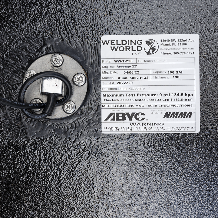 A white product label from "Welding World Inc." affixed to a textured black surface. The label provides details for a "Revenge 22'" fuel tank, including Part# WW-T-250, a manufacturing date of 04/06/22, material of Alum. 5052-H-32, a capacity of 100 gallons, and a thickness of .190. It also specifies a maximum test pressure of 9 psi / 34.5 kpa, and indicates compliance with ISO 8846 and 10088 specifications, as well as ABYC and NMMA memberships. A circular metallic component with wires and screws is visible