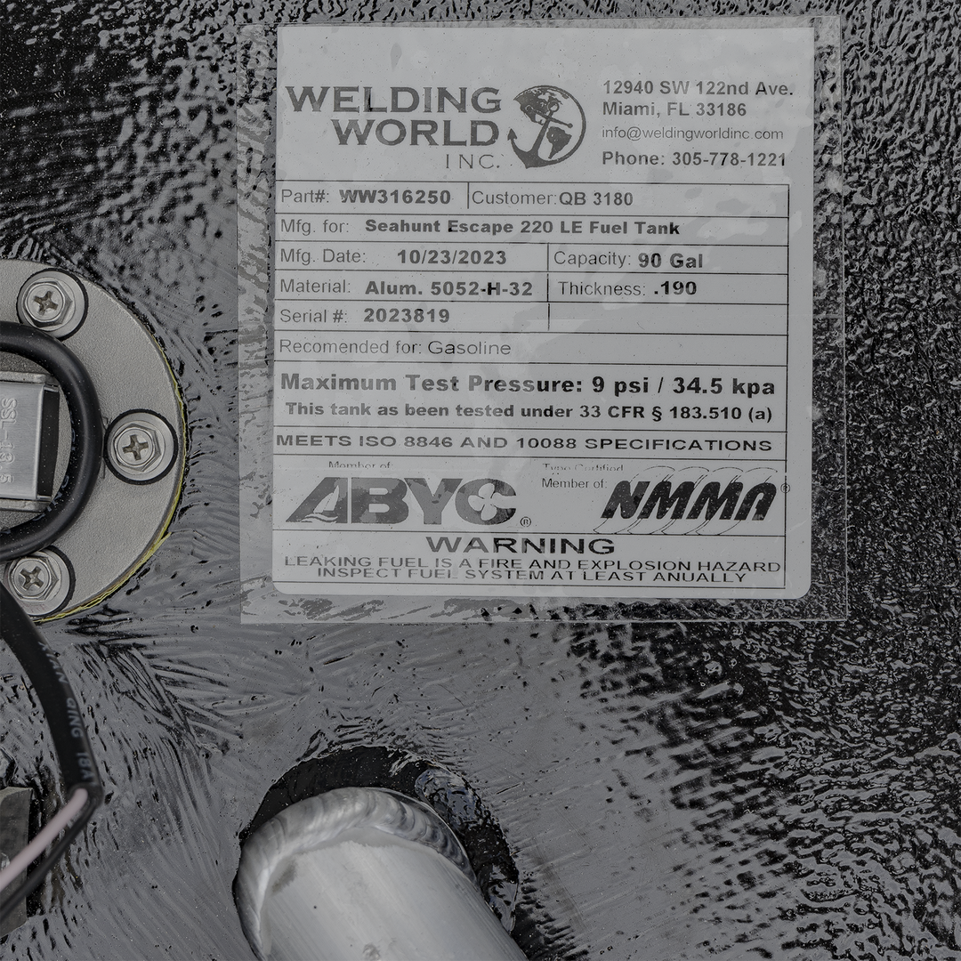 This is a close-up photo of a metal fuel tank label from Welding World Inc., located in Miami, Florida. The label includes the part number WW316250 and customer number QB 3180. It specifies that the tank is manufactured for the Seahunt Escape 220 LE Fuel Tank model, with a manufacturing date of October 23, 2023. The tank has a capacity of 90 gallons and is made from aluminum 5052-H-32 with a thickness of 0.190 inches. The serial number is 2023819.