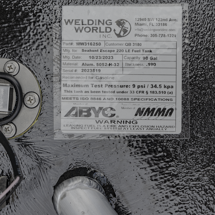 This is a close-up photo of a metal fuel tank label from Welding World Inc., located in Miami, Florida. The label includes the part number WW316250 and customer number QB 3180. It specifies that the tank is manufactured for the Seahunt Escape 220 LE Fuel Tank model, with a manufacturing date of October 23, 2023. The tank has a capacity of 90 gallons and is made from aluminum 5052-H-32 with a thickness of 0.190 inches. The serial number is 2023819.