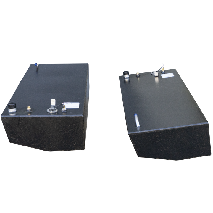 Two rectangular, dark grey fuel tanks, with various caps and fittings on their top surfaces, are positioned against a checkered black and grey background. The tanks appear to be made of metal, possibly aluminum