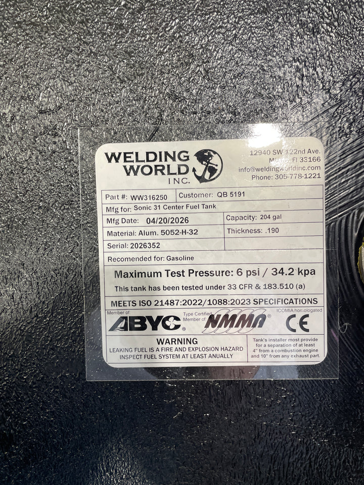 Close-up photograph of the Welding World Inc. manufacturing tag for a Sonic 31 Center fuel tank replacement. The label specifies a 204-gallon capacity, heavy-duty .190" thickness 5052-H32 aluminum construction, and a 6 psi maximum test pressure. It certifies compliance with ABYC, NMMA, CE, and USCG 33 CFR § 183.510(a) safety standards, ensuring a high-quality, legally compliant OEM replacement for marine gasoline systems.