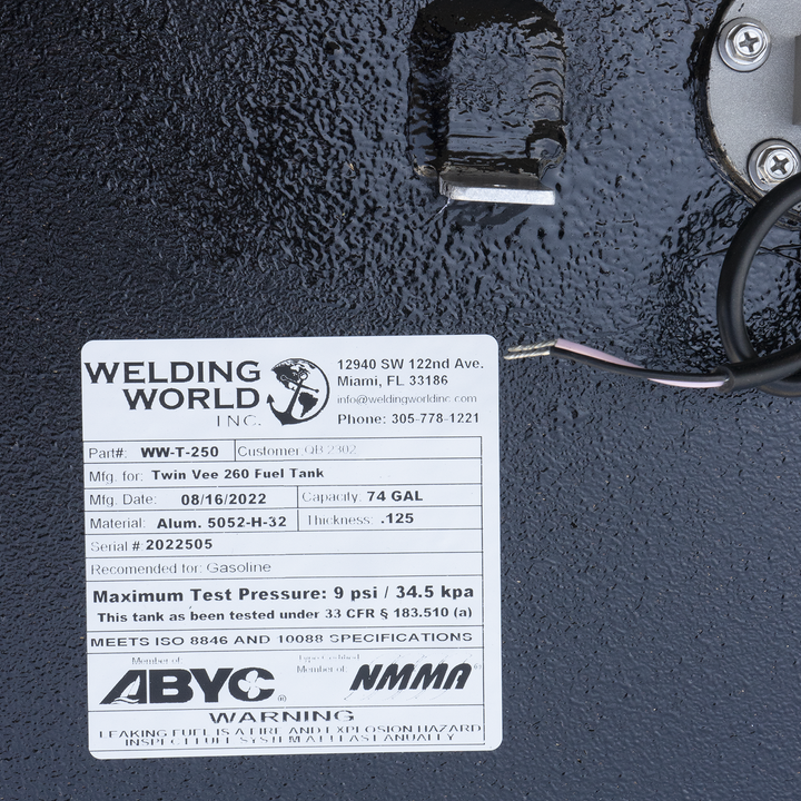 "A close-up view of a product label from 'Welding World Inc.' attached to a textured black surface. The label provides detailed specifications for a 'Twin Vee 260 Fuel Tank,' including Part # WW-T-250, Mfg. Date 08/16/2022, Capacity 74 GAL, Material Alum. 5052-H-32, Thickness .125, and Serial # 2022505. It also states the tank is recommended for Gasoline, has a Maximum Test Pressure of 9 psi / 34.5 kpa, and meets ISO 8846 and 10088 specifications. Logos for ABYC and NMMA are present