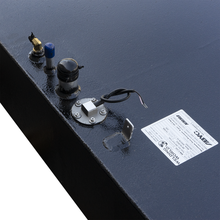 A close-up, angled view of the top surface of a textured black fuel tank, displaying several fittings and a partial view of a product label. Visible components include a brass elbow fitting, a blue-capped cylindrical pipe, a black domed sensor with a ribbed base, and a circular fuel level sending unit with exposed wires. A silver L-shaped bracket is also present, and a white 'Welding World Inc.' product label is partially visible in the bottom right corner