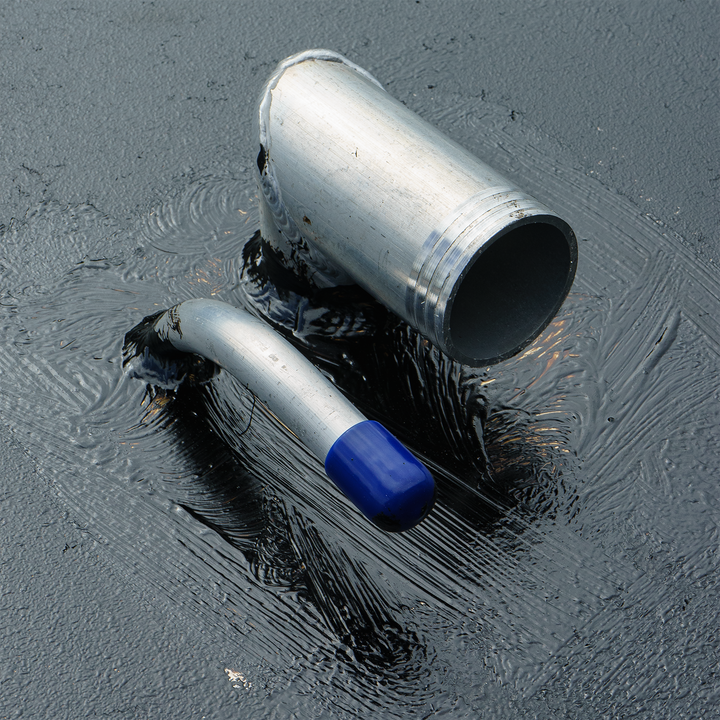 Close-up of a silver aluminum fuel tank fitting with a blue cap, resting on a dark, textured surface