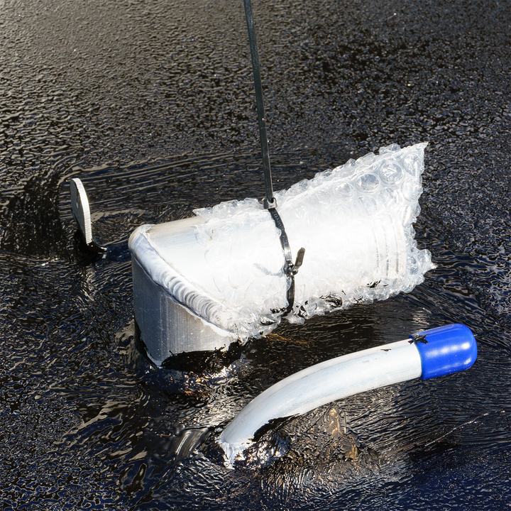 A Wellcraft Scarab 302 OEM replacement fuel tank partially submerged in water, with a protective bubble wrap covering and a fuel line attached