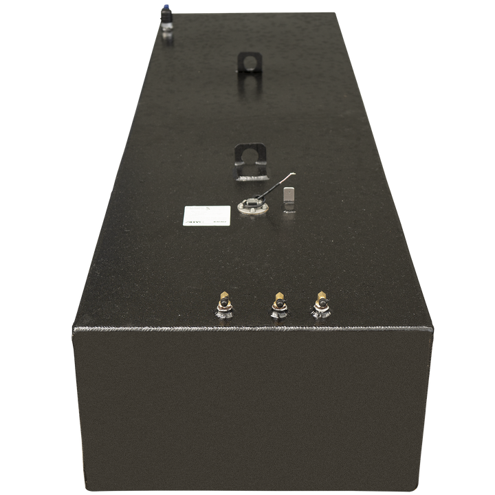 A long, black, rectangular fuel tank with a textured surface, shown from a slightly elevated, front-facing angle. The top of the tank features several components: three brass-colored fittings along the front edge, a small white label, a circular sensor with wires, a small rectangular component, and two curved metal mounting brackets. A blue-capped vent is visible at the far end of the tank